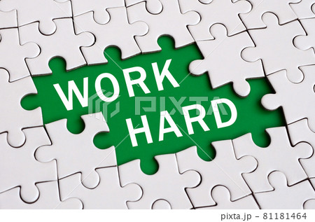 White jigsaw puzzle in assembled state with missing elements forming a green space with white inscription. Work hard 81181464