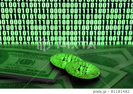 Two bitcoins lies on a pile of dollar bills on the background of a monitor depicting a binary code of bright green zeros and one units on a black background. Low key lighting 81181482