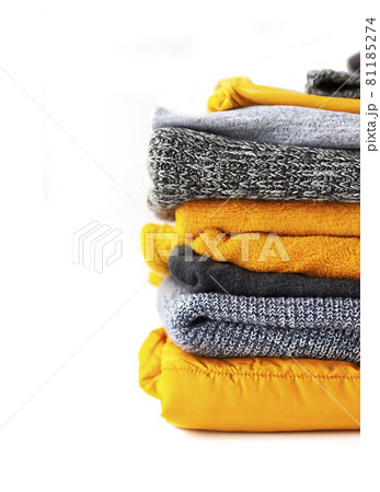 Pile of the warm knitted clothes. Warm yellow and grey sweaters and jumpers in stack on white background. 81185274