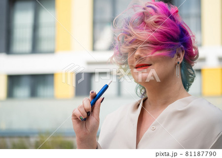 Caucasian woman with colored hair smokes an electronic cigarette. 81187790