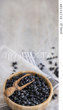 Wooden bowl full of dried black beans with a wooden spoon on kitchen towels close up 81191588