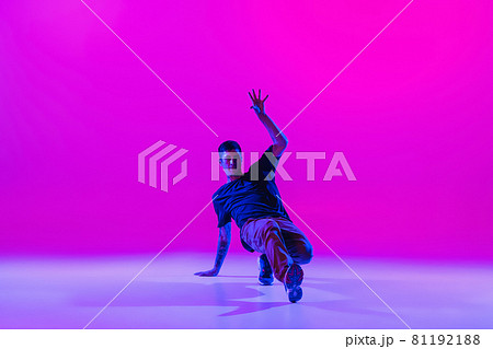Young stylish man, hip-hop dancer dancing solo in modern clothes isolated over bright magenta background at dance hall in neon light. 81192188