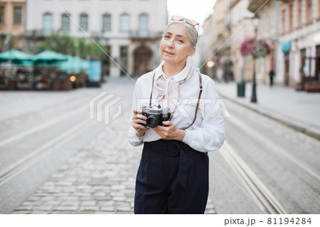 Mature woman posing outdoors with retro camera in hands 81194284