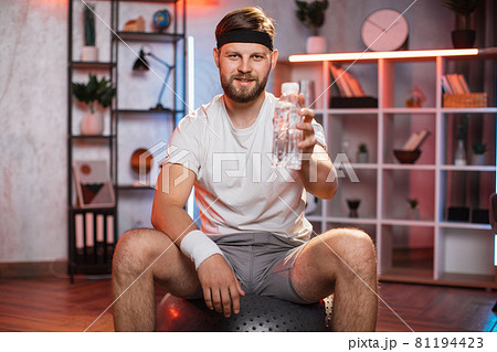 Smiling man holding bottle of water while sitting on fitball Smiling man holding bottle of water while sitting on fitball 81194423