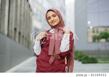 Arab female doctor or medical student, posing and smiling, standing outside modern clinic 81194433