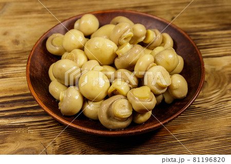Ceramic plate with pickled champignons. Marinated mushrooms on wooden table 81196820