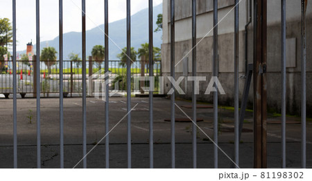 A view through a steel fence, onto another fence and a part of the volcano sakurajima in the distance. A view through a steel fence, onto another fence and a part of the volcano sakurajima in the distance. 81198302