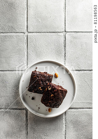 Chocolate Zucchini brownie on a white plate on a gray tile background Chocolate Zucchini brownie on a white plate on a gray tile background 81198563