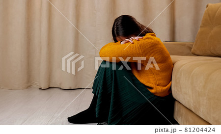 Depressed lady in sweater and skirt sits on wooden floor Depressed lady in sweater and skirt sits on wooden floor 81204424