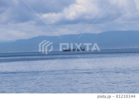 雲の多い空とタンカーの行く海と対岸の山と街がぼんやり霞んで見える風景 81210144