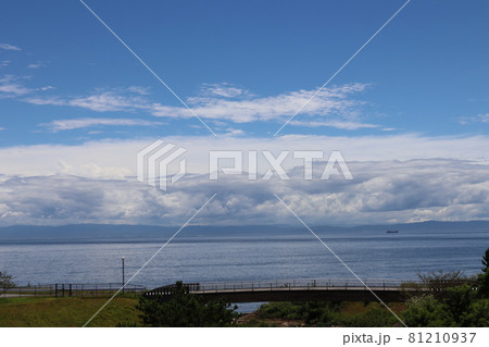 もくもくした灰色の雲と白い雲と青空と道路の橋と船の行く海とぼんやり霞んで見える対岸の山のある風景 もくもくした灰色の雲と白い雲と青空と道路の橋と船の行く海とぼんやり霞んで見える対岸の山のある風景 81210937