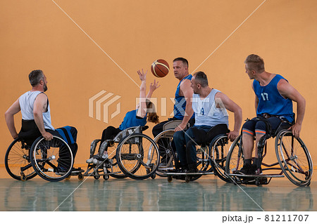 Disabled War veterans mixed race opposing basketball teams in wheelchairs photographed in action while playing an important match in a modern hall.  81211707
