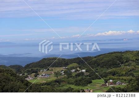 高台から見た山と田畑と民家と道と青い海とぼんやり霞んで見える島々と雲の多い青空のある風景 高台から見た山と田畑と民家と道と青い海とぼんやり霞んで見える島々と雲の多い青空のある風景 81212388