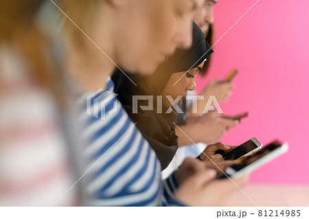 diverse teenagers use mobile devices while posing for a studio photo in front of a pink background diverse teenagers use mobile devices while posing for a studio photo in front of a pink background 81214985