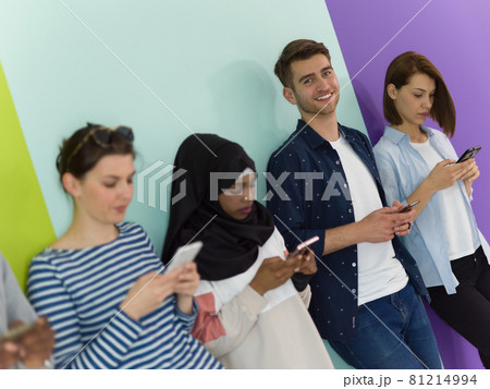 diverse teenagers use mobile devices while posing for a studio photo in front of a pink background 81214994