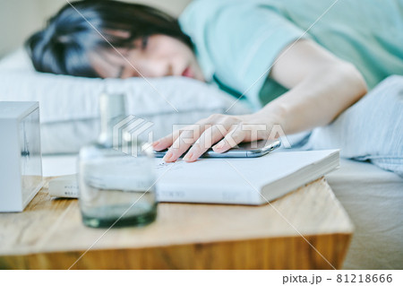 朝起きてスマホを手に取ろうとする女性 朝起きてスマホを手に取ろうとする女性 81218666