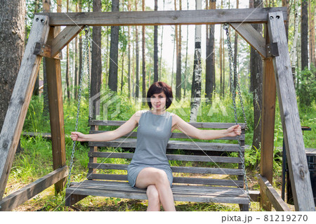 A happy brunette in a striped dress rides on a swing in a birch grove A happy brunette in a striped dress rides on a swing in a birch grove 81219270