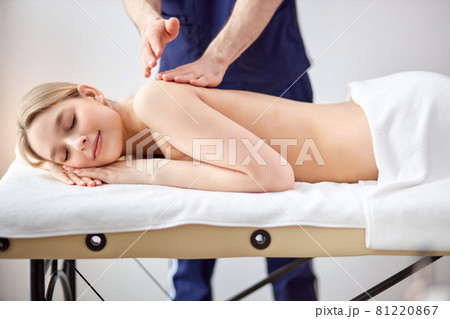 Gorgeous lady lying on tummy receiving massage on back by cropped male therapist Gorgeous lady lying on tummy receiving massage on back by cropped male therapist 81220867