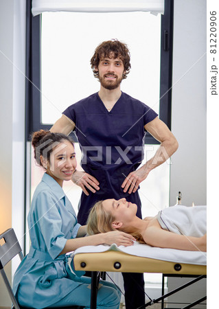 Two caucasian masseurs practice massaging on female client face and head Two caucasian masseurs practice massaging on female client face and head 81220906