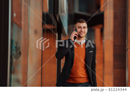 Going to airport terminal. Confident businessman traveler walking on city streets and pulling his suitcase drinking coffee and speaking on smartphone 81224344