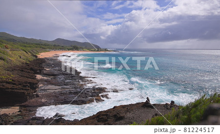 People swim in the turquoise waters of the Tropical Beach. Sandy Beach. Blue Waves of the Pacific Ocean Beats Oahu Island Volcanic Cliffs. Ke One Kula Lookout. Clear sunny day. DCI 4k 81224517