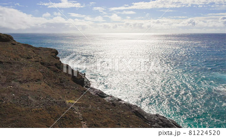 Sunrise over the island of Oahu. White clouds float across the blue sky. Blue Waves of the Pacific Ocean Beats Oahu Island Volcanic Cliffs. Turquoise water color. Clear sunny day. DCI 4k 81224520