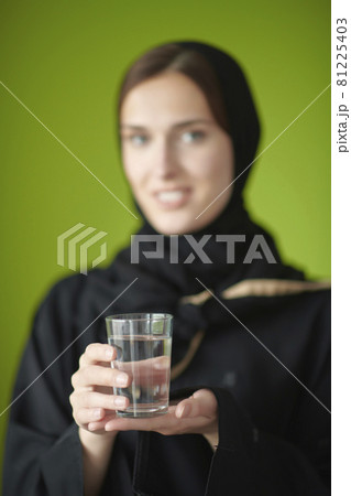 Middle eastern woman in abaya holding a glass of water Middle eastern woman in abaya holding a glass of water 81225403