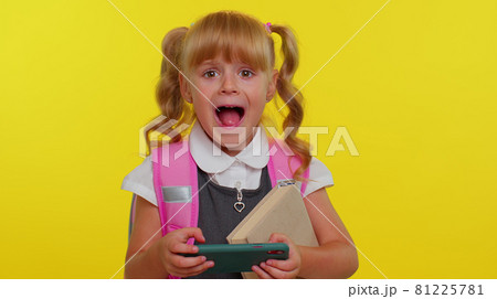 Funny exited school girl wear backpack enthusiastically playing racing video games on mobile phone 81225781