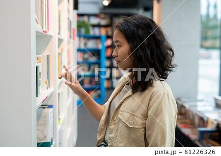 Young businesswoman or student standing by one of shelves with books 81226326