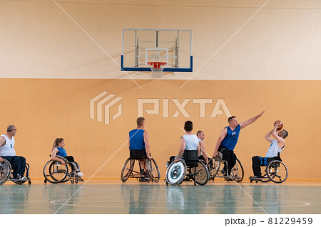 Disabled War veterans mixed race opposing basketball teams in wheelchairs photographed in action while playing an important match in a modern hall.  81229459