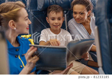 Female flight attendant entertaining a kid on board by offering a book to read. Cabin crew provide service to family in airplane Female flight attendant entertaining a kid on board by offering a book to read. Cabin crew provide service to family in airplane 81233185