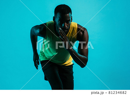 Portrait of an athlete against a blue background in position to start a run 81234682