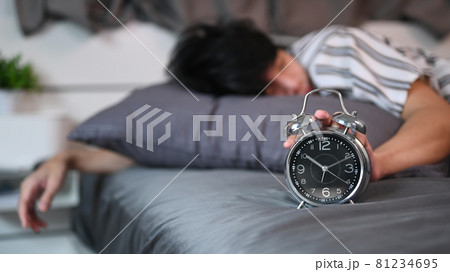 Asian man lying on his bed and stopping alarm clock. 81234695