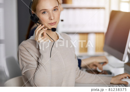 Friendly caucasian businesswoman talking by headset in sunny office. Call center and diverse people group in business 81238375