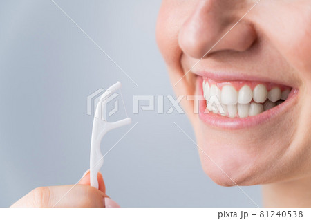 Close-up portrait of a beautiful caucasian woman with a flawless smile holding a toothpick with dental floss on a white background Close-up portrait of a beautiful caucasian woman with a flawless smile holding a toothpick with dental floss on a white background 81240538