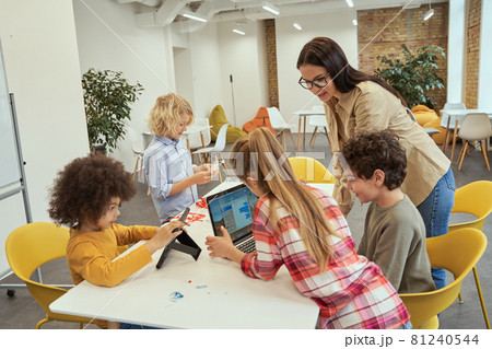 Fun and engaging. Happy children using gadgets during STEM class with young female teacher 81240544