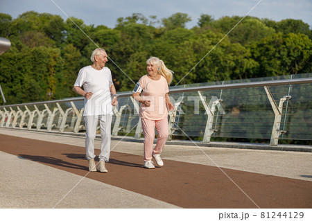 Happy senior man and woman run together along footbridge in summer 81244129