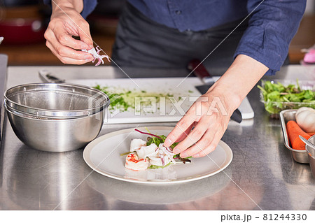 エビとイカを盛り付けるエプロン姿の若い男性　料理男子イメージ 81244330