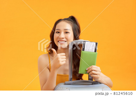 Portrait of an excited young woman holding passport with flying tickets with a suitcase isolated over yellow background 81245610