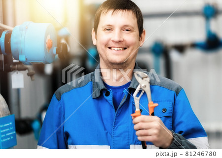 A plumber or equipment adjuster holds a wrench in his hand and smiles. Portrait of a real Caucasian 81246780