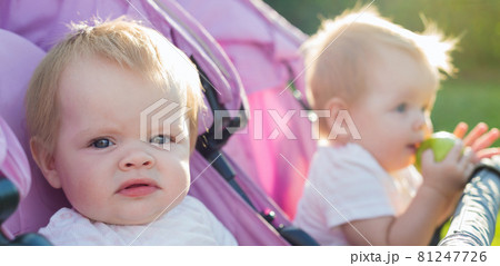 Portrait of Caucasian twin children of 6 months of age with blonde hair sitting in a baby carriage Portrait of Caucasian twin children of 6 months of age with blonde hair sitting in a baby carriage 81247726