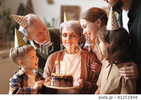 Happy senior woman holding cake with burning candles while celebrating birthday with big lovely family Happy senior woman holding cake with burning candles while celebrating birthday with big lovely family 81251948