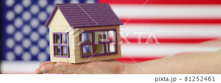 Small house with keys on hand against background of American flag Small house with keys on hand against background of American flag 81252461