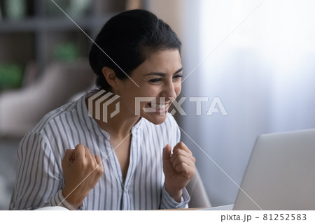 Overjoyed Indian woman triumphs reading good news on laptop 81252583