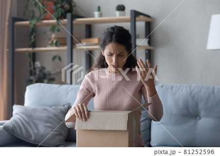 Woman unpacking box feels dissatisfied by received post parcel Woman unpacking box feels dissatisfied by received post parcel 81252596