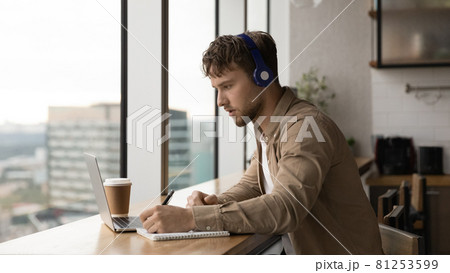 Man listens audio taking notes making assignment use laptop Man listens audio taking notes making assignment use laptop 81253599