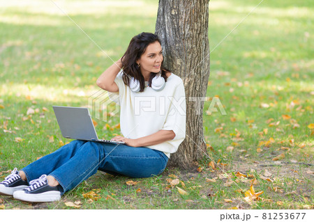 Photo of a 40-year-old woman with laptop sitting on a grass in city park. Photo of a 40-year-old woman with laptop sitting on a grass in city park. 81253677