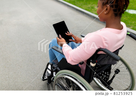 Young black impaired woman in wheelchair using tablet computer with empty screen at autumn park, mockup Young black impaired woman in wheelchair using tablet computer with empty screen at autumn park, mockup 81253925