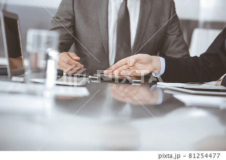 Unknown businessman using tablet computer and working together with his colleague while sits at the glass desk in modern office. Teamwork and partnership concept Unknown businessman using tablet computer and working together with his colleague while sits at the glass desk in modern office. Teamwork and partnership concept 81254477