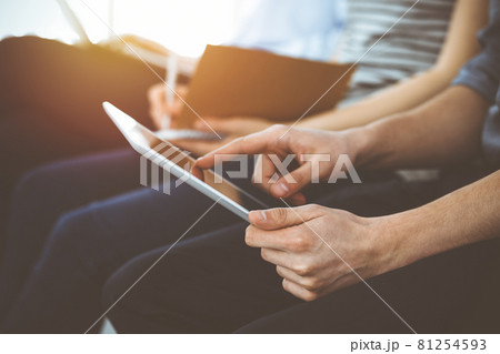 Group of casual dressed business people working at meeting or conference in sunny office, close-up of hands. Businessman using tablet computer Group of casual dressed business people working at meeting or conference in sunny office, close-up of hands. Businessman using tablet computer 81254593